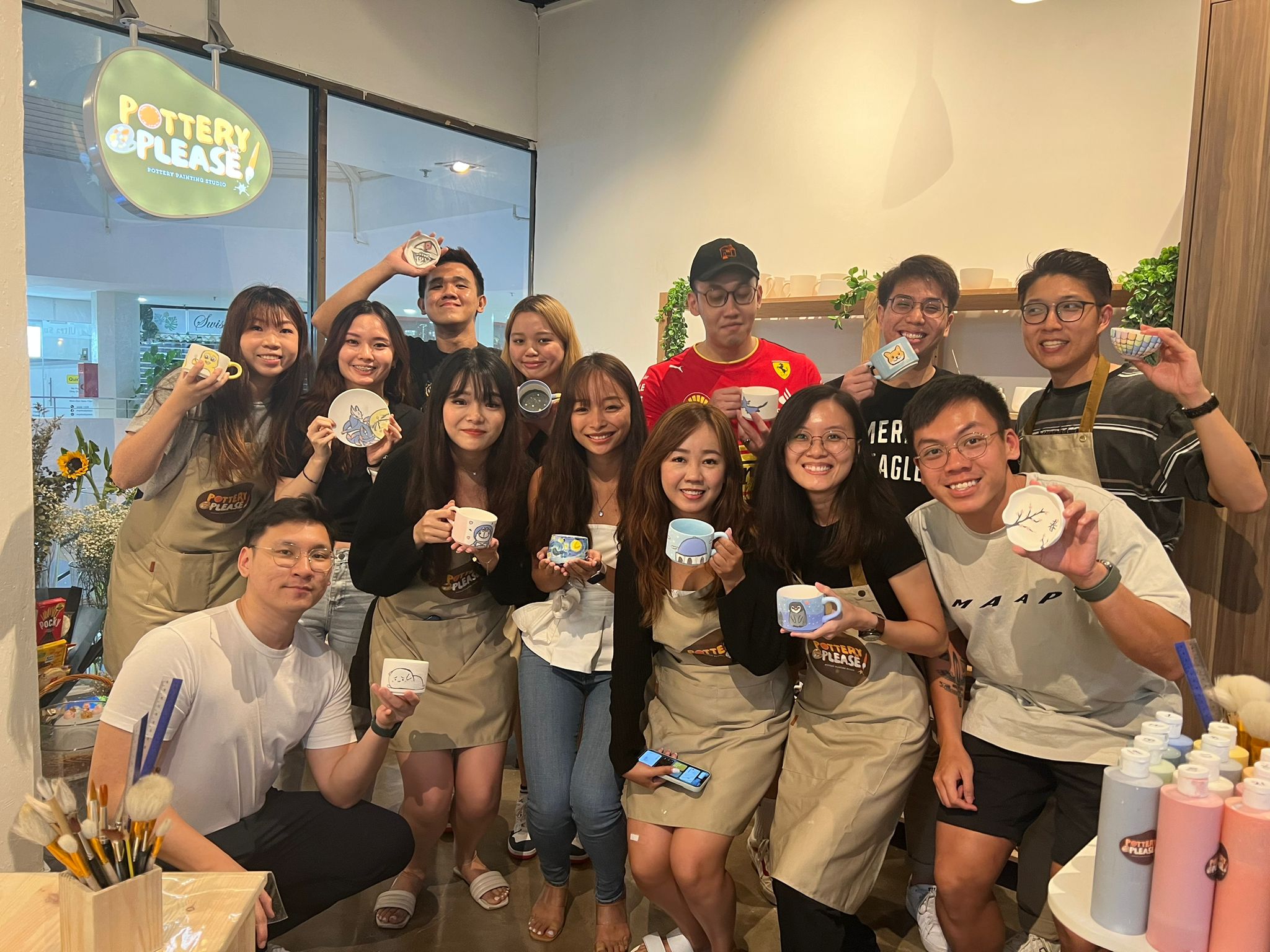 Smiling group posing with their finished pottery pieces after a client appreciation pottery painting session at PotteryPlease!